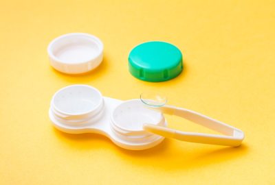 Contact lens on tweezers over an open container for storing and cleaning lenses