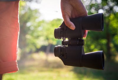 Male hiker looking through binoculars in forest